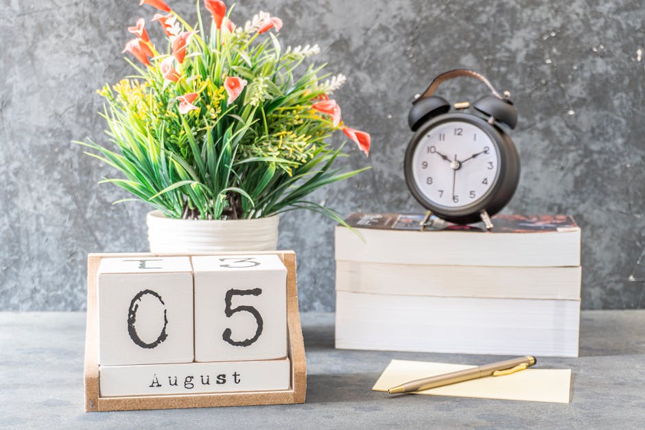 Stylish decorative arrangement featuring a calendar, clock, books, and a flower vase on a wooden surface.