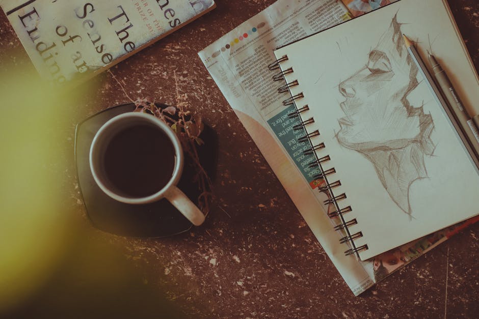 From above of sketchbook with person portrait near pen and pencil next to mug with drink on saucer with herbs on table near book and newspaper in light room