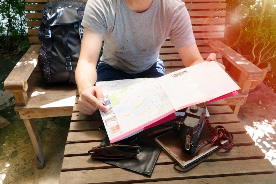 Young traveler examining a map on a sunny bench with travel gear, including a camera and backpack.